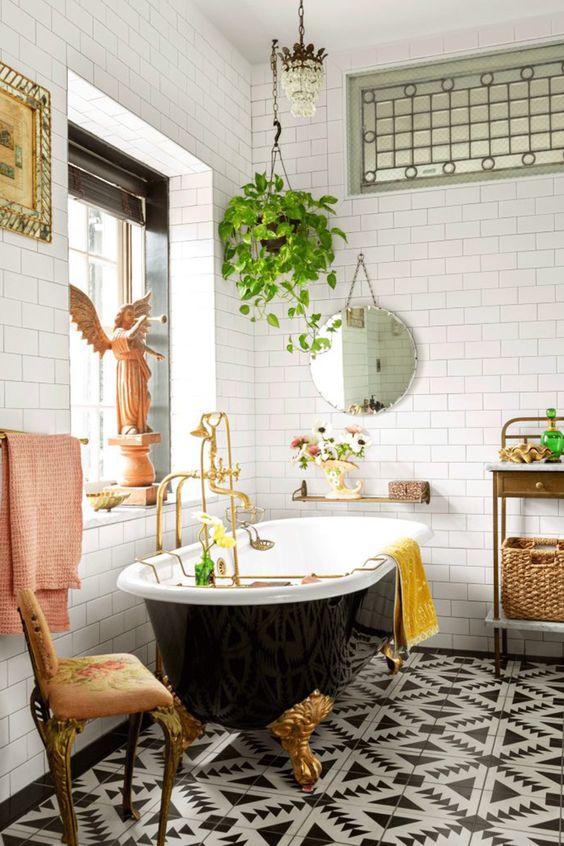 a fancy and whimsy bathroom with a gorgeous printed tile floor, a black vintage tub, a crystal chandelier and vintage furniture and a potted plant