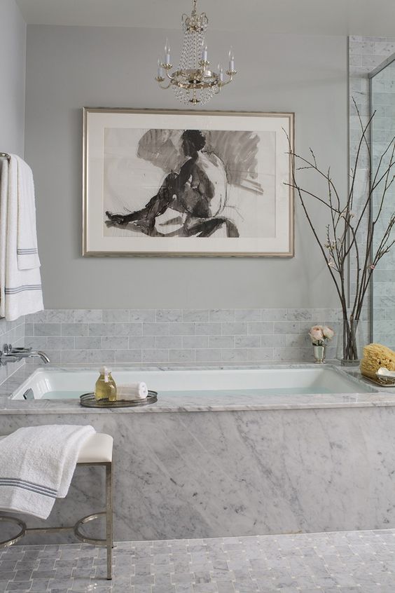 a fancy bathroom with grey marble tiles and marble itself, a crystla chandelier and a bold statement artwork just wows