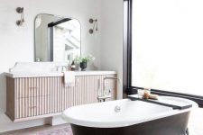 a fancy bathroom with white walls and a neutral tiled floor, a black vintage bathtub, a floating vanity and a pendant lamp plus a frosted glass wall