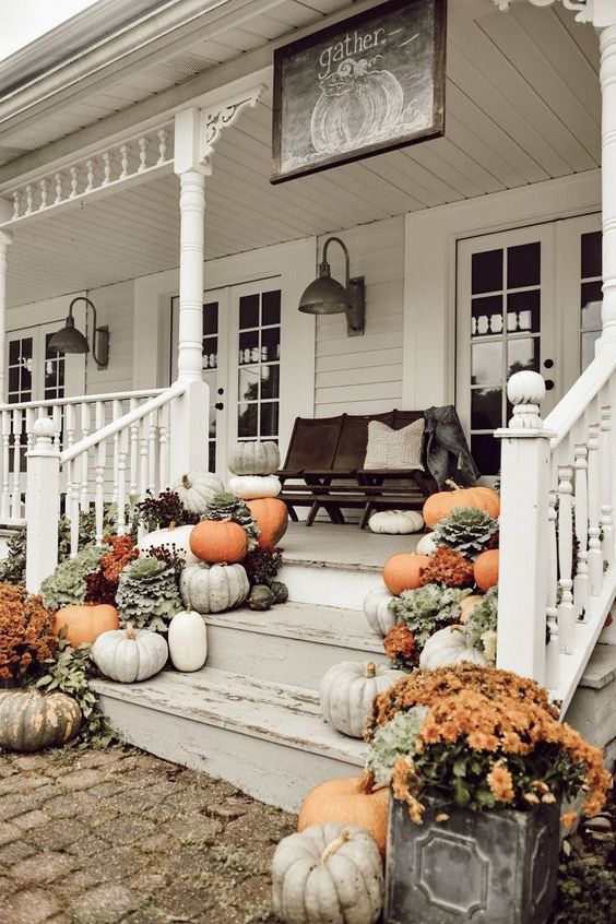 a farmhouse fall porch with a black bench and lots of pillows, pumpkins, blooms and greenery and vintage sconces on the walls