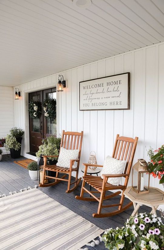 a farmhouse porch styled for summer, with wooden rockers, potted plants, a sign and a rug is a very welcoming and cool space