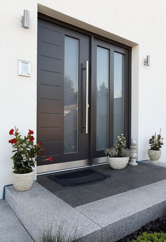 a large modern black door with glass inserts, three planters with blooms and greenery on the porch