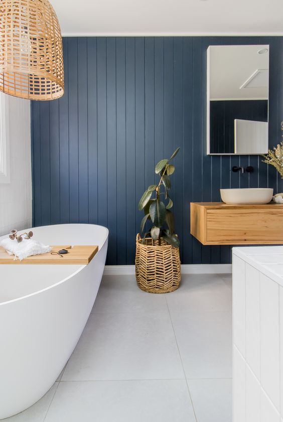 a lovely modern country bathroom wiht a navy planked accent wall, a floating vanity, white appliances and a woven lamp and a planter is great