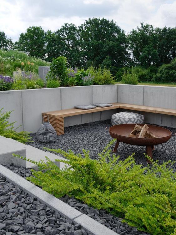 a lovely modern sunken patio with gravel on the ground, a bench and a fire pit plus greenery growing around to refresh the look