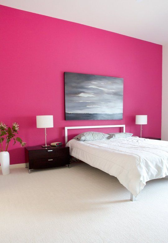 a minimal bedroom with a hot pink accent wall, a white bed, black nightstands, a statement artwork and some white lamps