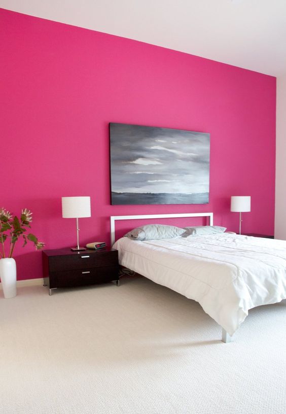 a minimalist bedroom with a hot pink accent wall, a simple bed and nightstands, a table lamp and a moory artwork