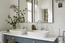 a modern country bathroom with white planked walls and a tiled floor, a double grey vanity, two tall mirrors and some greenery