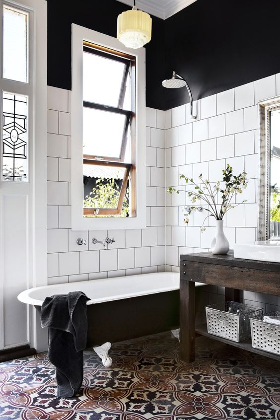a modern country bathroom with white square and bright mosaic tiles, a black clawfoot tub, a dark stained vanity, pendant lamps and greenery