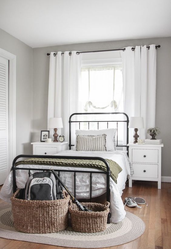 a modern country bedroom with a forged bed and white nightstands, baskets and a woven rug, neutral textiles and plants