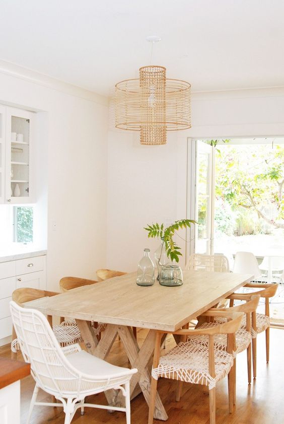 a modern country dining room with white buffets, a wooden trestle table and woven and rattan chairs plus a woven pendant lamp