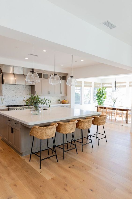 a modern country kitchen in dove grey, with shaker style cabinets, a large kitchen island, pendant lamp, woven stools