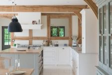a modern country kitchen in white, light blue and light grey, butcherblock countertops, wooden beams on the ceiling and pendant lamps