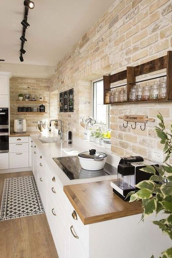 a modern country kitchen with exposed brick, white cabinets, white and butcherblock countertops and laminate flooring
