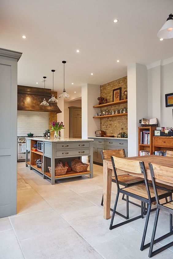 a modern country kitchen with exposed brick, white subway tiles, light grey cabinets and a kitchen island, pendant lamps and metallic fixtures