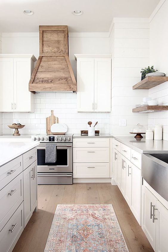 a modern country kitchen with shaker style cabinets, a white subway tile backsplash, a wooden hood and floating shelves