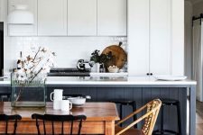 a modern country kitchen with white cabinets and a navy kitchen island, a vintage table and chairs for the dining space