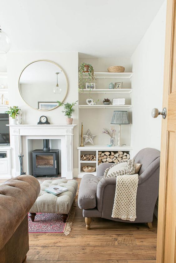 a modern country living room with a hearth, a grey sofa and an ottoman, a leather sofa, firewood, built-in shelves and potted plants