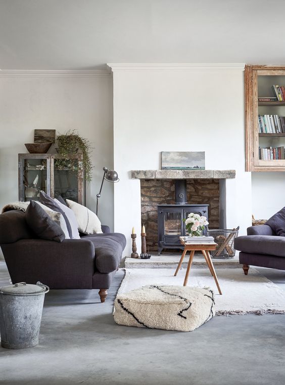 a modern country living room with a hearth, graphite grey furniture, a coffee table and a pouf, some vintage storage units