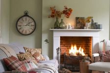 a modern country living room with light green walls, a fireplace, neutral furniture and printed textiles, a vintage clock and leaves