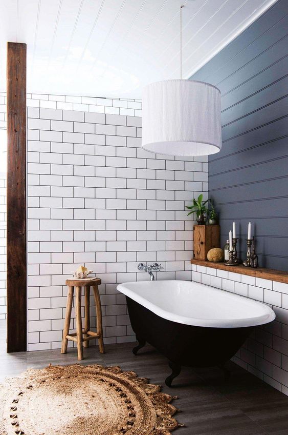 a modern country style bathroom with a navy planked wall and a subway tile one, a black vintage tub, a woven rug and a pendant lamp