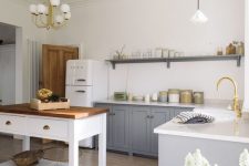 a modern country style kitchen with grey cabinets and a white kitchen island, pendant lamps and touches of gold