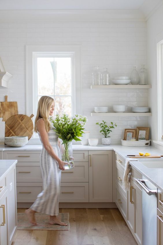 a modern creamy country style kitchen with shaker cabientry, white countertops and walls clad with white subway tiles plus open shelves