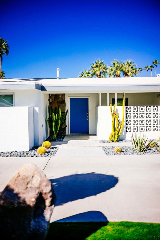 a modern desert entrance with a screen, a bold blue door, growing cacti and tiled pathways is a chic mid-century modern space