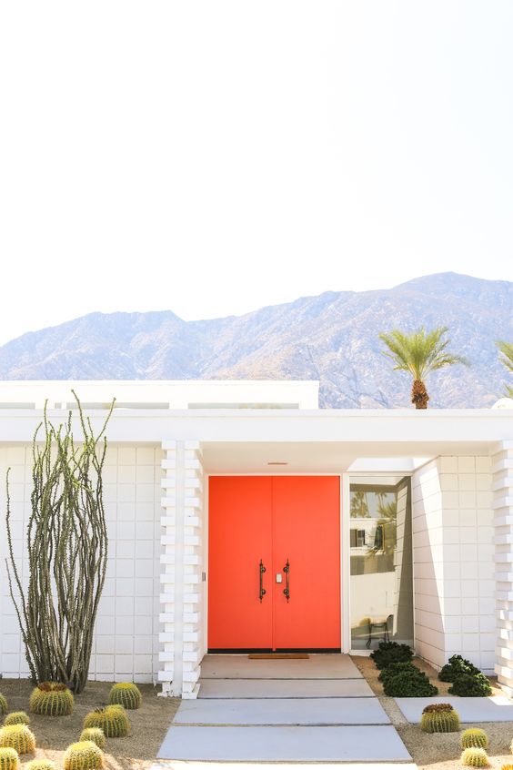 a modern entrance with fiery red doors, cacti and agaves, some greenery around the entrance is a cool space with a desert feel