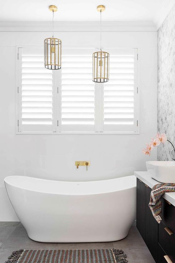 a modern fancy bathroom with a grey marble hex tile wall, an oval tub, a black vanity and gold pendant lamps and fixtures