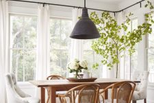 a modern farmhouse dining space with a stained table, woven and upholstered chairs, a potted tree, a black pendant lamp