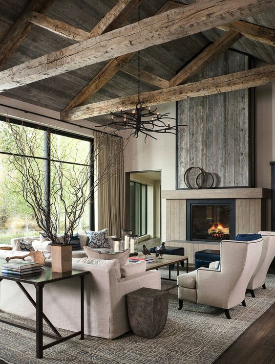 a modern farmhouse living room with a rough wooden ceiling and beams, a fireplace clad with wood, neutral furniture and a console