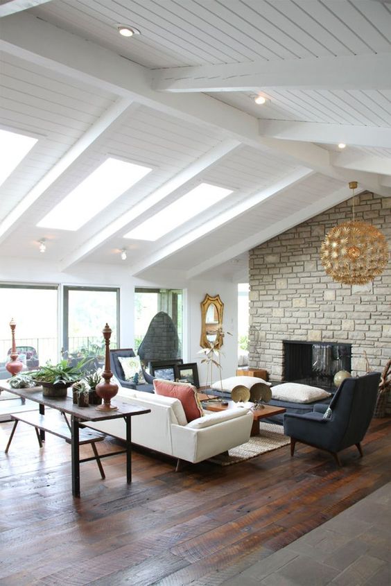 a modern farmhouse living room with a stone clad fireplace, neutral and dark furniture, a console and a bench plus a gilded lamp