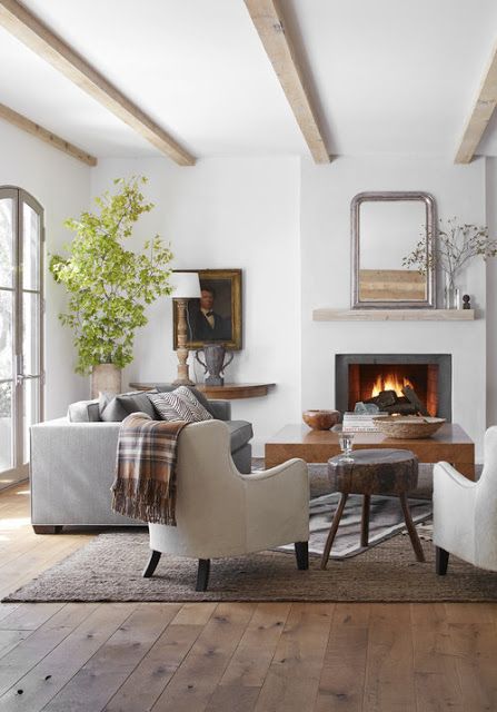 a modern farmhouse living space with a fireplace, neutral furniture, wooden coffee tables, wooden beams on the ceiling and a potted tree