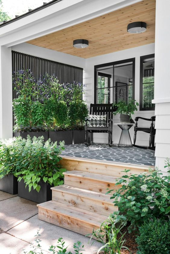 a modern farmhouse porch with a black printed rug, black rockers and printed pillows, potted plants and blooms is very cozy