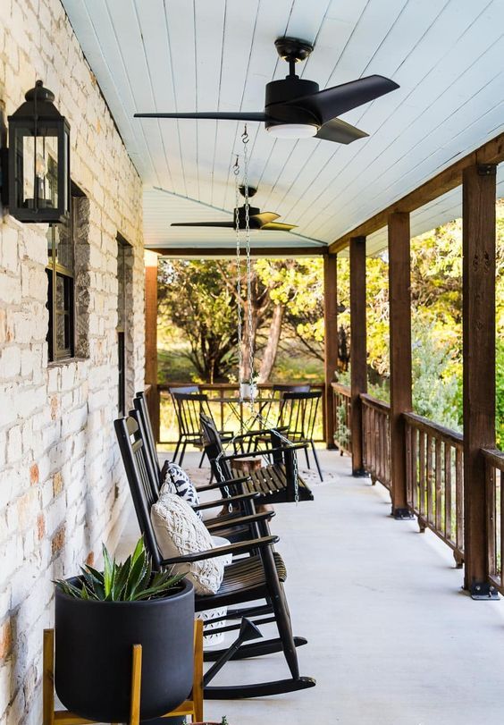 a modern farmhouse porch with black rockers and a bench on chains, modern black planters and chic lanterns on the walls