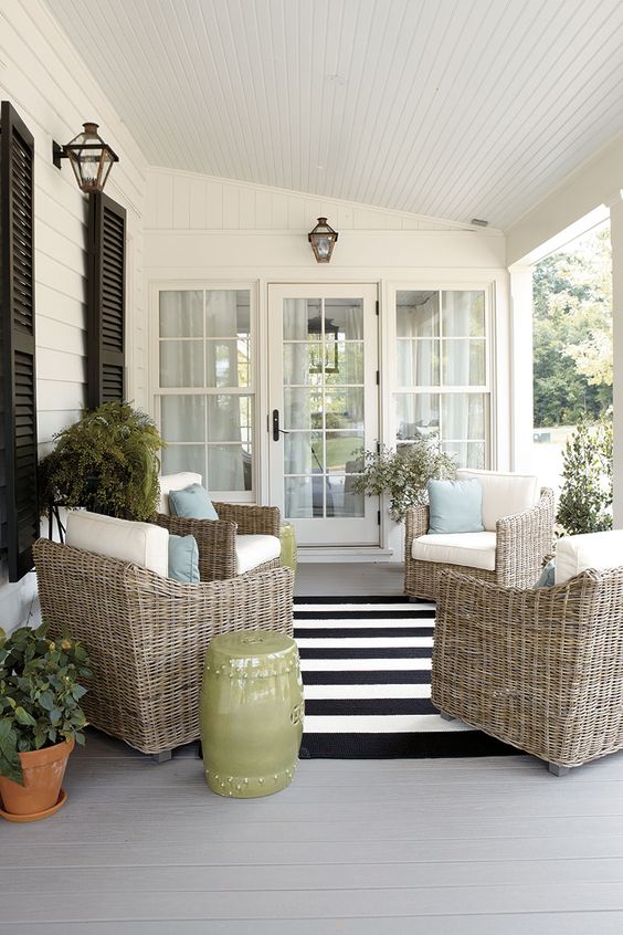 a modern farmhouse porch with elegant wicker chairs and pillows, potted greenery and blooms, a side table and cool lanterns