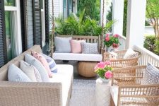a modern farmhouse porch with wicker furniture, printed pillows, a suspended bench, potted blooms and greenery is welcoming