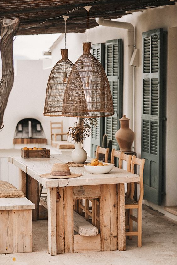 a modern farmhouse terrace with a roof and woven lamps, with a rough wood dining set and a hearth is a lovely space to have a meal