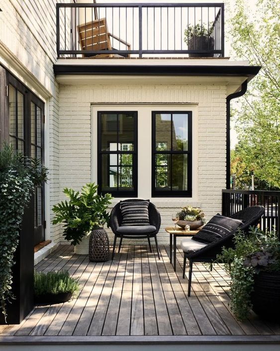 a modern front porch with a deck, black chairs with pillows, a side table, potted greenery and candle lanterns is cool