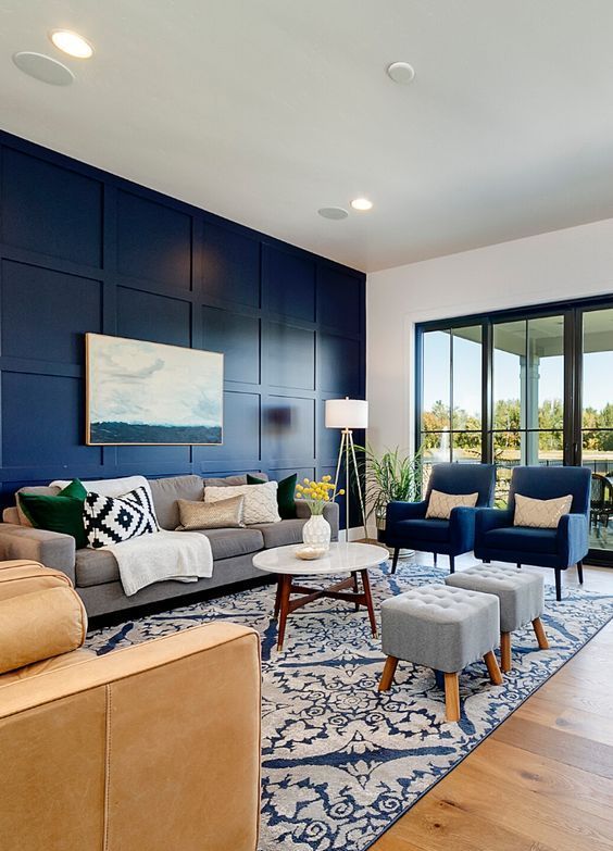 A Modern Living Room With A Navy Paneled Wall Chic Grey And Navy Furniture A Tan Sofa A Printed Rug And Blankets 