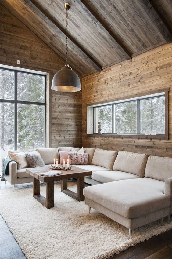 a modern rustic living room fully clad with wood, with a large neutral sectional, a coffee table and a pendant lamp