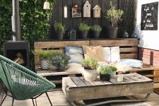 a modern rustic terrace with a pallet bench, pretty textiles, a pallet coffee table, a green chair and a hearth plus potted greenery