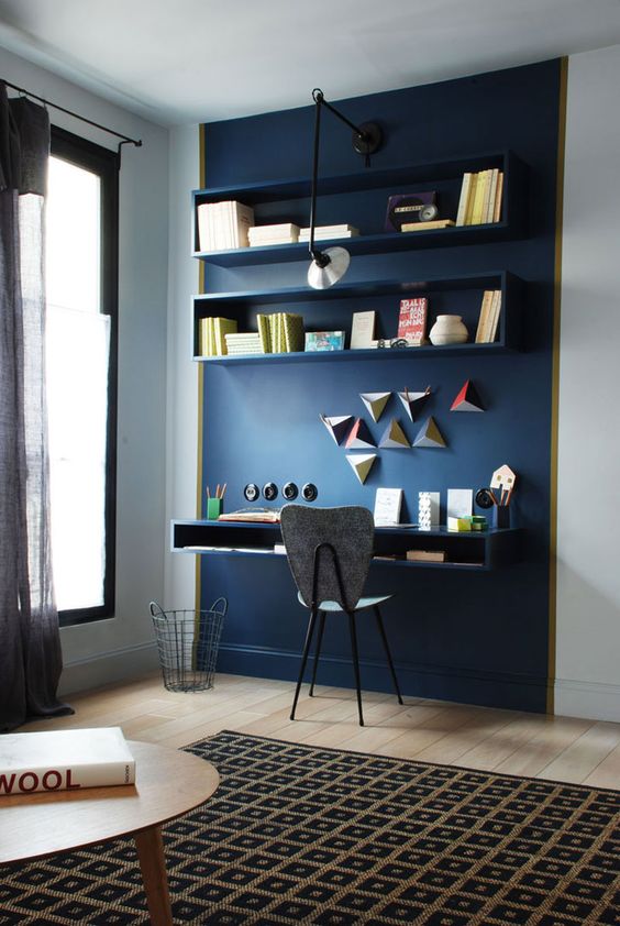 a navy accent wall that highlights the home office nook, with open shelves and geometric decor, with a floating desk and a grey chair