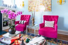 a quirky living room with light blue walls, hot pink chairs, yellow sconces, a glass table with books and hot pink orchids