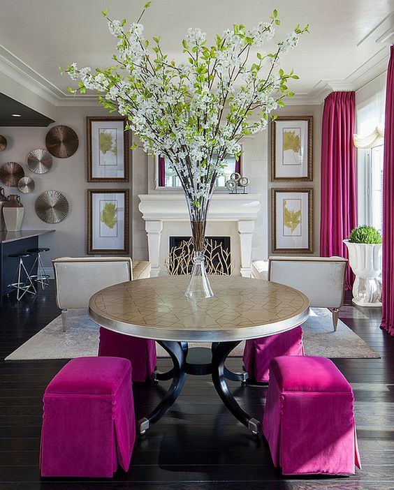 a refined space done in neutrals, with a fireplace clad with beautiful screen, hot pink curtains and a round mirror with hot pink poufs