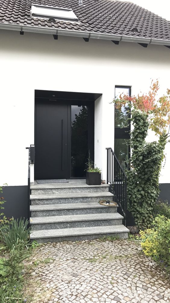 a simple modern front porch with a black door, a concrete ladder, potted greenery and plants around is amazing