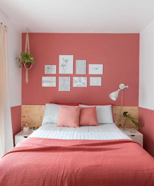 a small and bold bedroom with a salmon pink accent wall plus matching bedding, some potted plants and a cool white sconce is pure chic