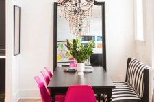 a sophisticated dining room with a black table, a striped bench, hot pink chairs, a chic black chandelier and a floor mirror