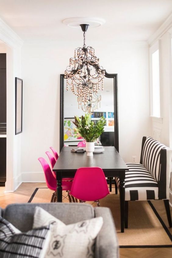a sophisticated dining room with a black table, a striped bench, hot pink chairs, a chic black chandelier and a floor mirror