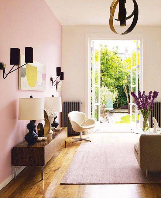 a stylish living room with a pink accent wall, some chic furniture in modern style, a catchy chandelier and black sconces